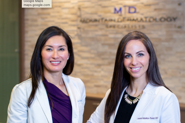 Dr. Jean Liu Urquhart and Dr. Lauren Meshkov Bonati wear white doctor's coat as they stand in front of the reception desk at Mountain Dermatology Specialists in Edwards, Colorado.