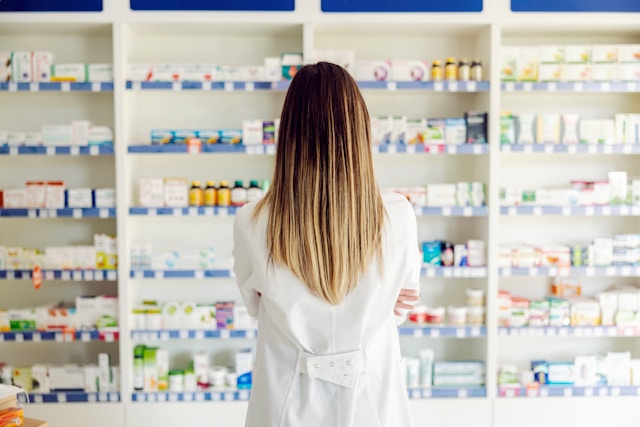 Female pharmacist with her back to the camera standing in front of shelves of medication.